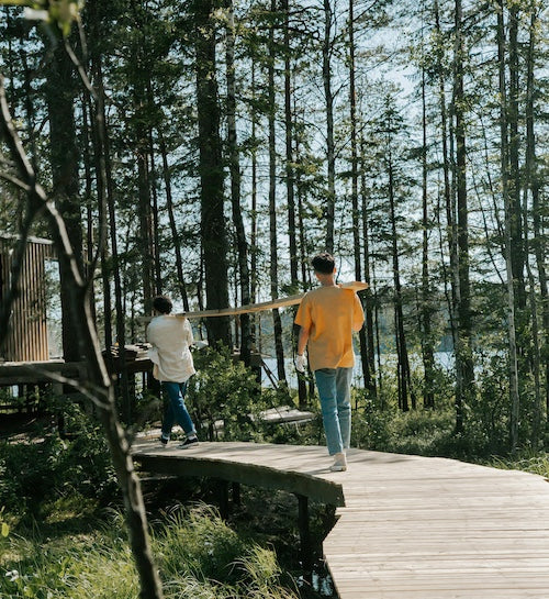 Two men carrying sauna lumber walking across a wooden boardwalk to build a sauna.