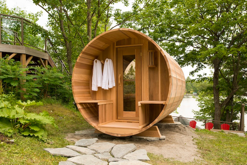 A custom, clear red cedar barrel sauna with a porch from Henki in Muskoka.