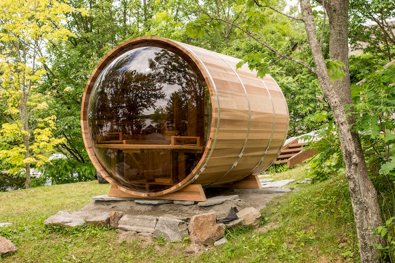 The back of a Henki Custom Barrel Sauna with a large dome window on patio stones.