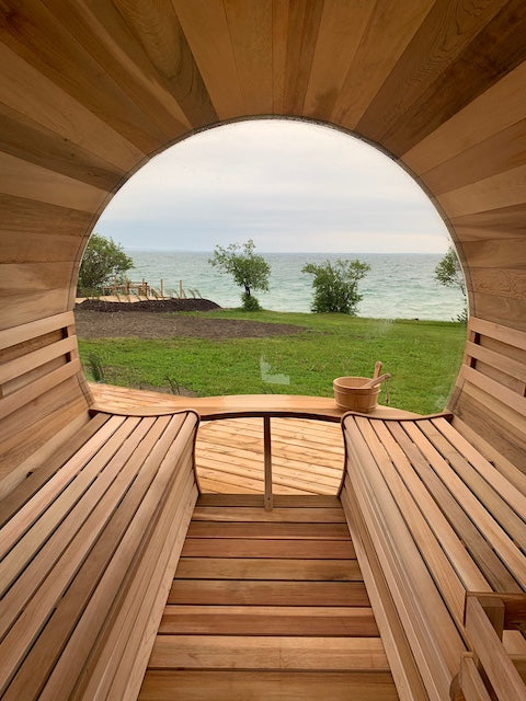 The inside of a Henki Custom Barrel Sauna  with a large dome window overlooking a grass lawn and lake Ontario.