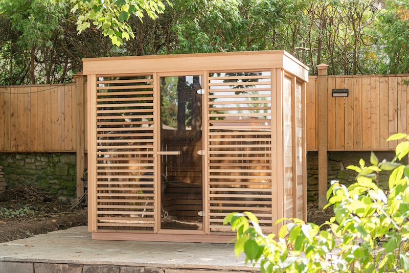 A Custom Pure Cube Sauna on a stone patio with green leaves in the foreground.