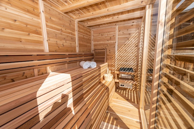 The interior of a Custom Pure Cube Sauna with two towels, a bucket, ladle, and a Henki Lumbar Back Rest on the benches.