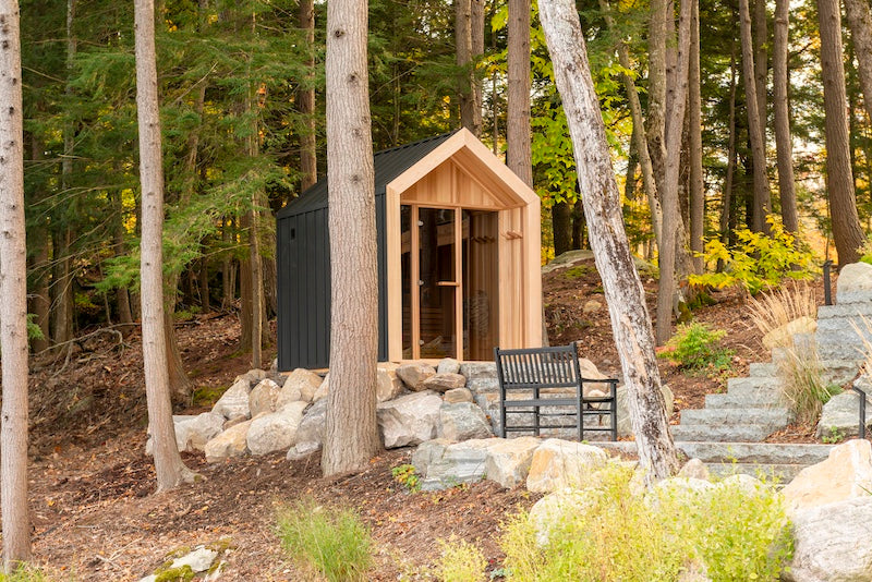 A Pure Cube Hudson Sauna on a cottage property with stone steps next to a forest.
