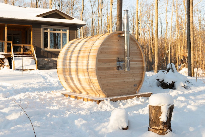 The back of a Henki Modern Barrel Sauna in the winter with a chimney coming out of the back wall.
