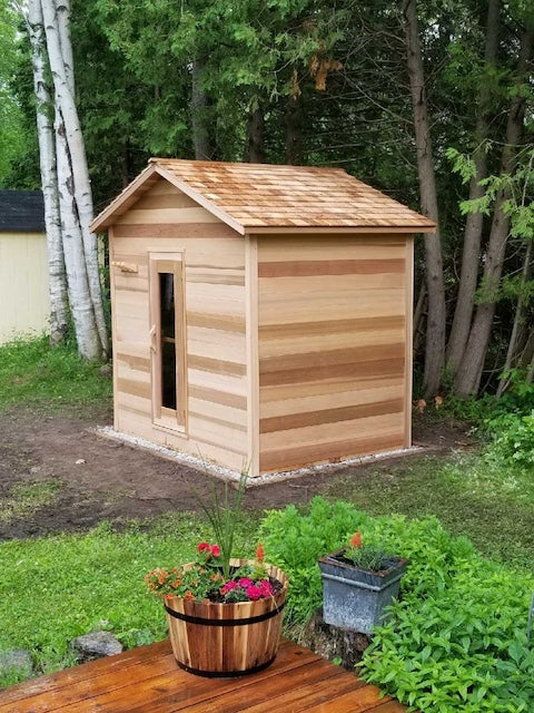 The clear cedar exterior of Henki Modern Cabin Sauna taken from a porch with a flower pot at the end of it. 