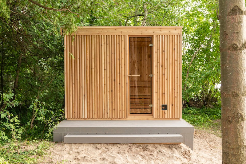 The side of a Pure Cube Neptune Sauna with fluted cedar siding and a full glass door.