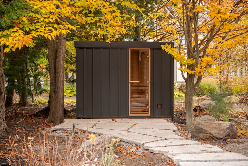 The side of a Pure Cube Neptune Sauna with black metal siding and a stone walkway leading up to it.