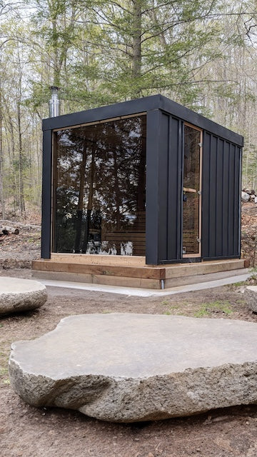A Pure Cube Neptune Sauna from Henki Sauna Co with large rocks in front of it.