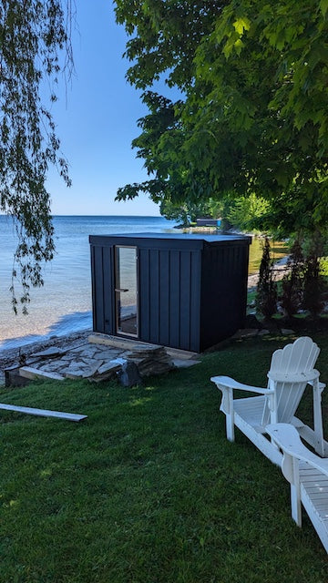 The side and back of a Neptune Sauna next to a lake in Canada.