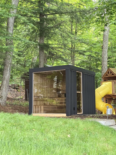 A Pure Cube Neptune Sauna in a backyard next to a playground with a yellow slide. 