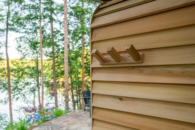 The edge of a Henki Panoramic Cube Sauna with Henki's Triple Cedar Towel Hook mounted on the bevel siding.