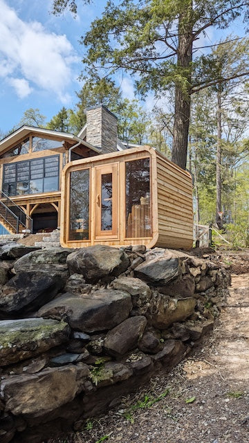 A Henki Panoramic Cube Sauna on rocks in front of a home.