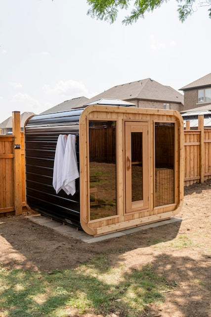 A Henki Panoramic Cube Sauna with black metal siding in a backyard in Ontario.