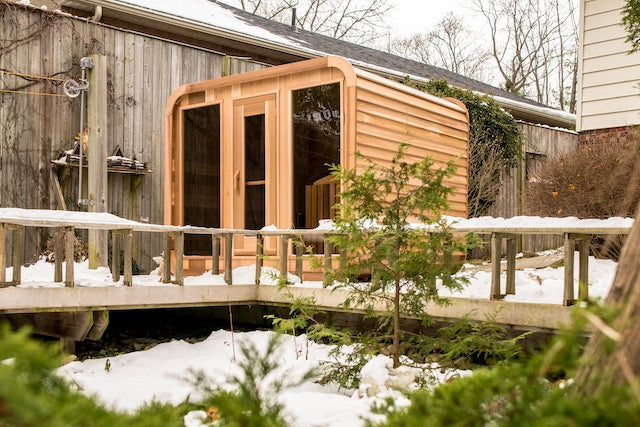 A Henki Panoramic Cube Sauna behind benches on a deck in the Canadian winter.