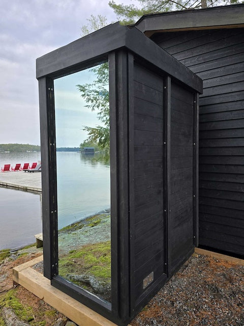 The back and side of a black Pure Cube Trinity Sauna next to a lake in Alberta. 